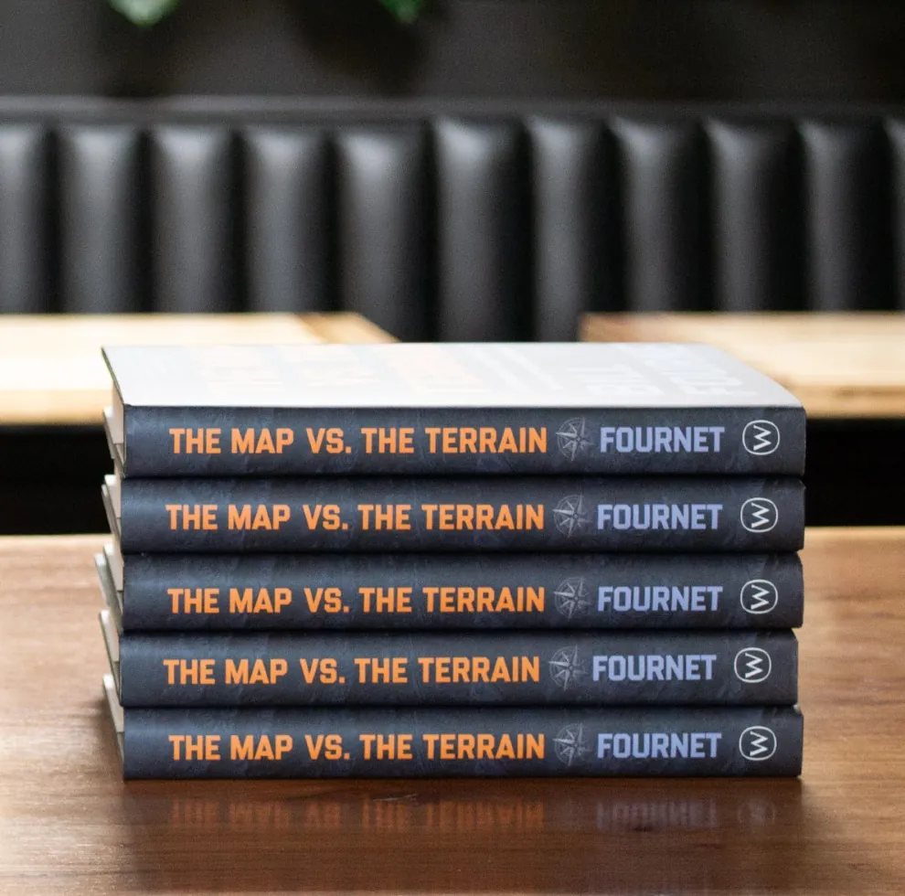 A stack of five hardcover copies of The Map vs. the Terrain on a wooden table
