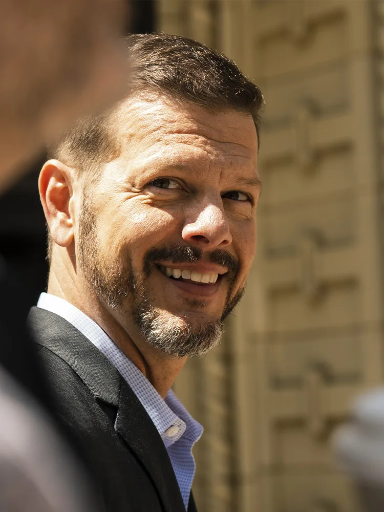 Bill Fournet smiling, in a sport coat, on a sunlit downtown street