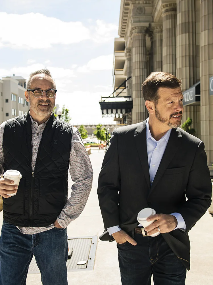 Bill Fournet walking and talking with a client on a downtown street, coffee in hand