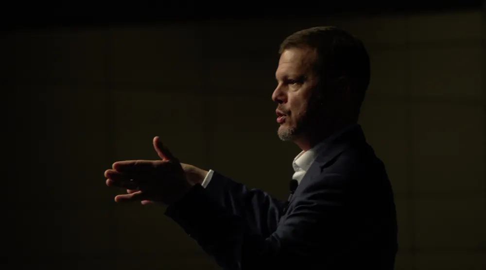Bill Fournet in profile, mid-sentence, gesturing under a spotlight