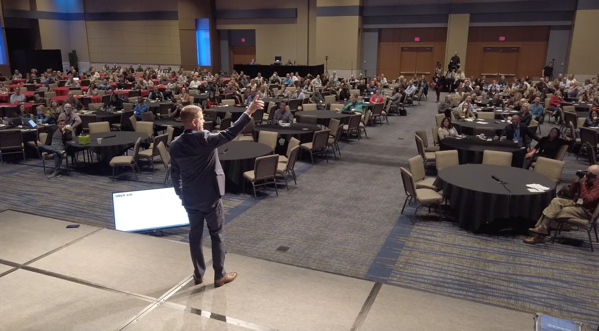 Bill Fournet on stage, arm raised, facing a packed ballroom