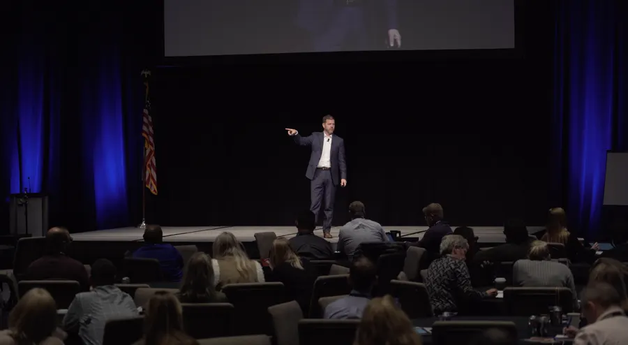 Bill speaking on a large stage beneath a projection screen
