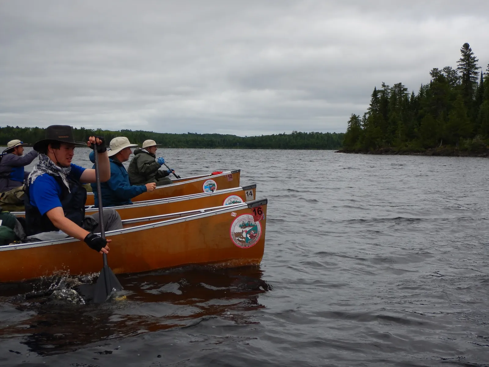 Three canoes of paddlers heading across a wind-rippled northern lake